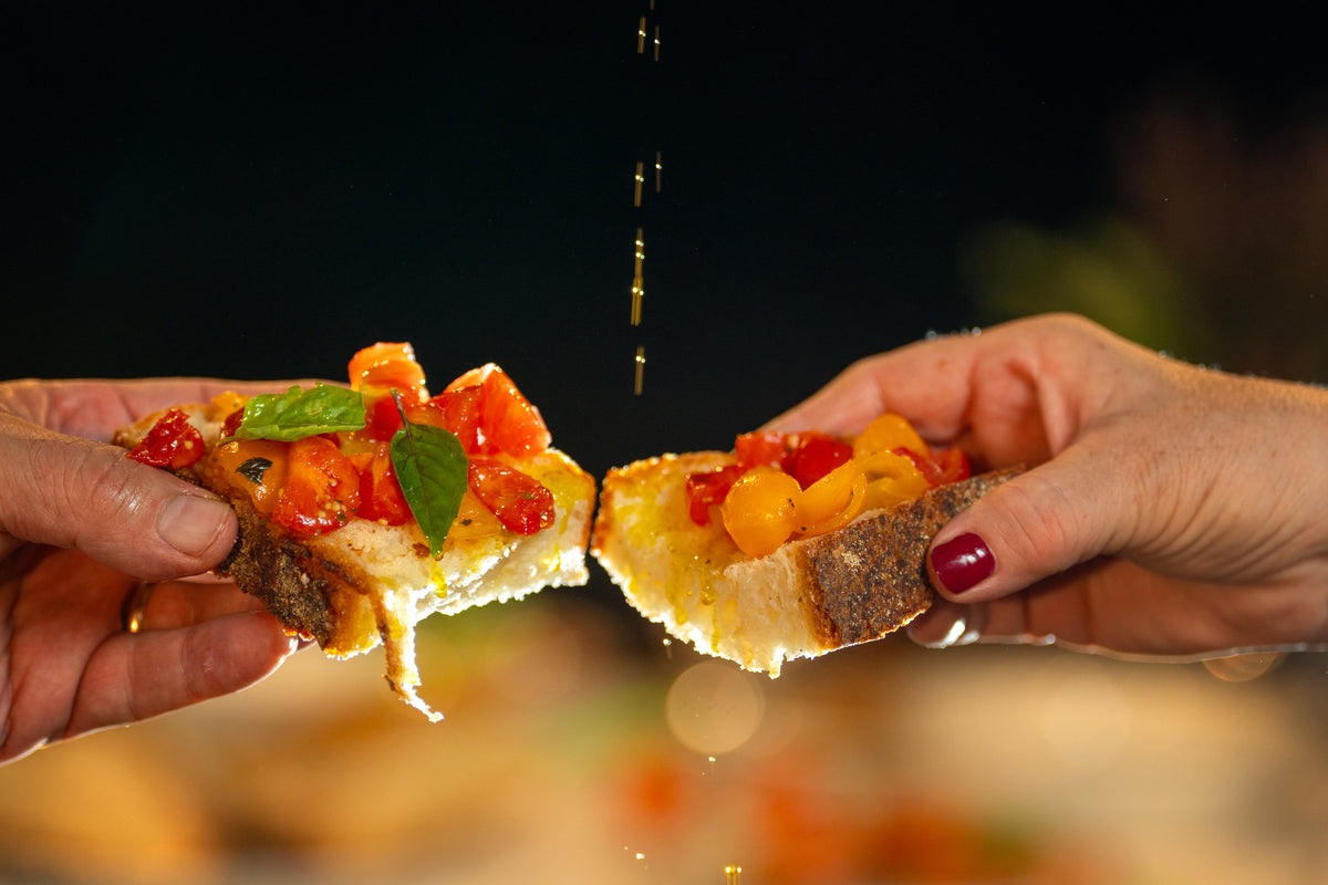 Mani che si passano una bruschetta con pomodoro e olio, a tavola