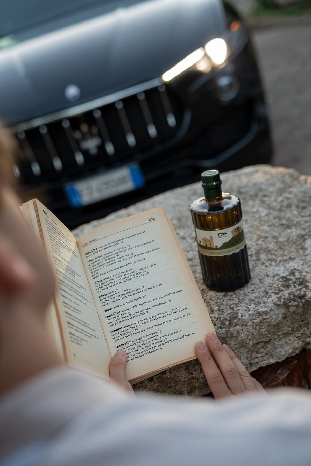 La bottiglia di Tenuta Grieci ,su un tavolo di pietra antico  ,mentre un sogegtto sfoglia un libro antico in contemplazoone di un capolavoro di meccanica aitaliana .